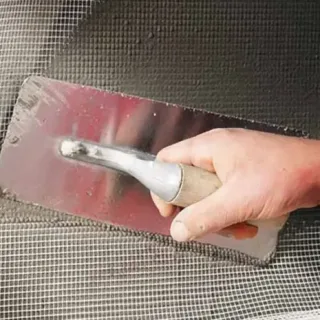 A trowel bedding fiberglass mesh into fresh render on a wall