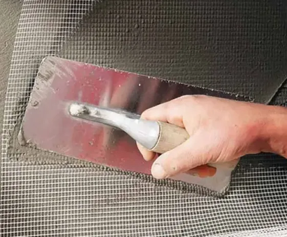 A trowel bedding fiberglass mesh into fresh render on a wall